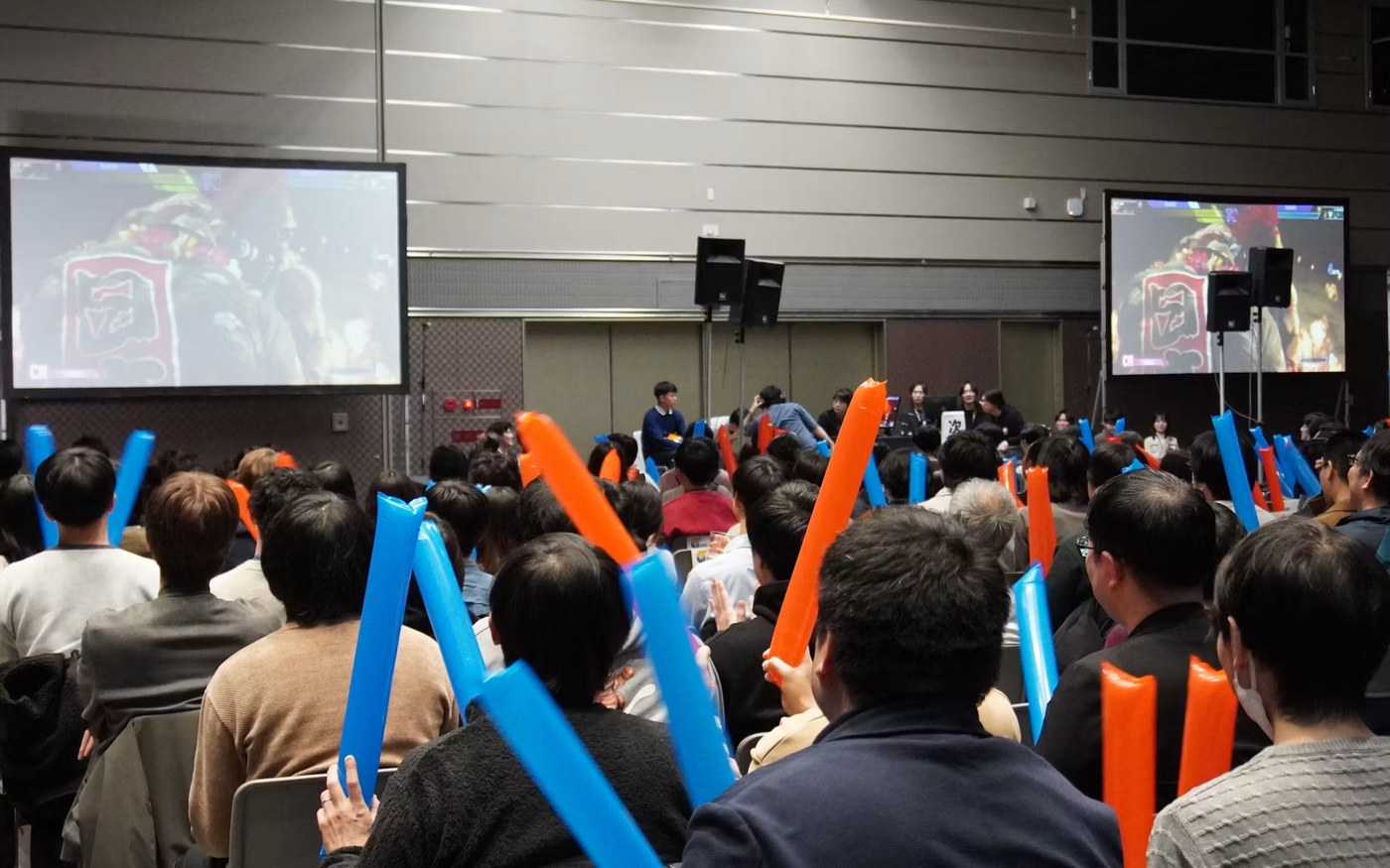 カプコンの社員向けeスポーツ大会の会場。スクリーンの試合を社員がスティックバルーンを持って応援している